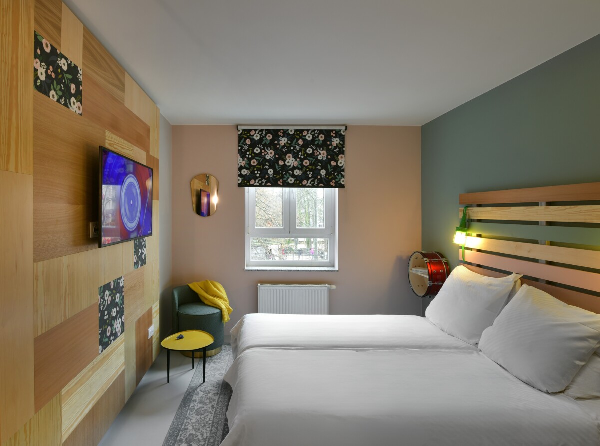Hotel room with double bed, wooden headboard, decorative drum, TV, and floral accents